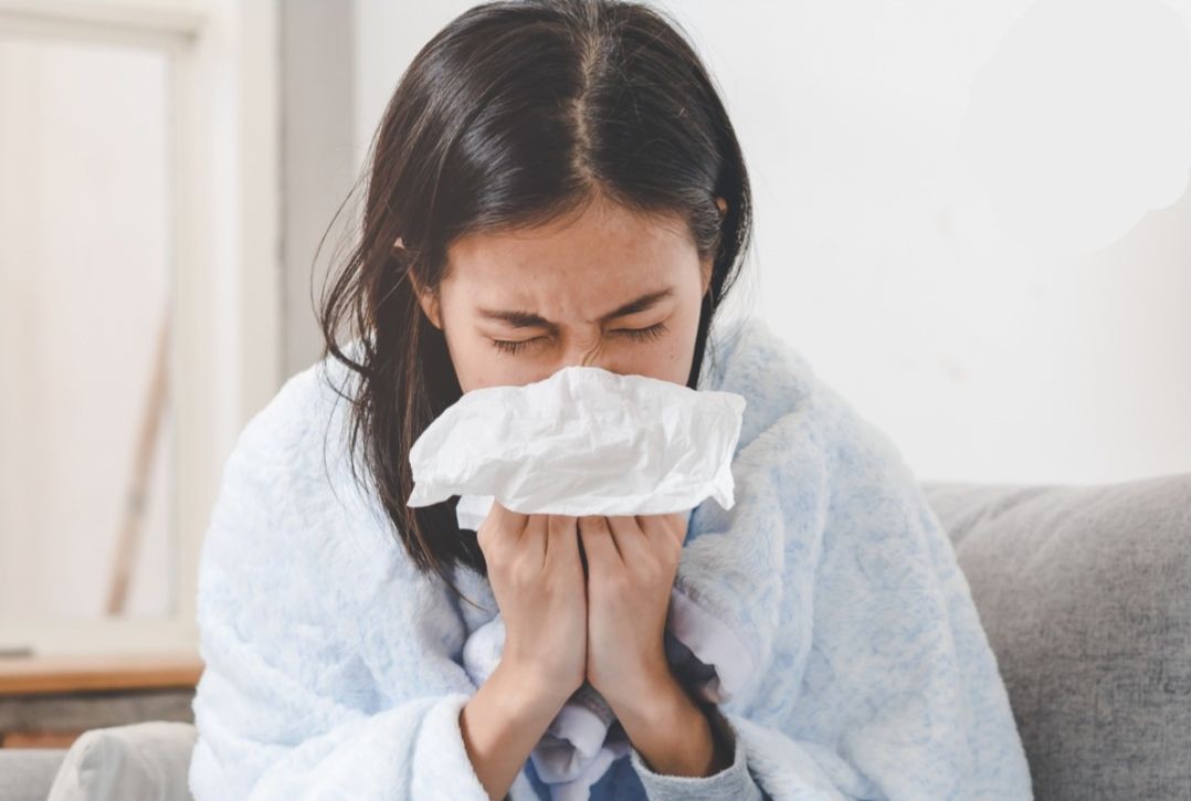 Image of woman blowing her nose with a blanket wrapped around her shoulders