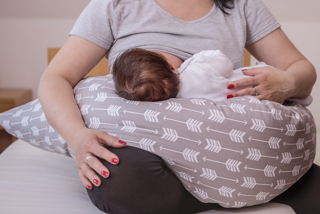 Torso of mom with a long pillow on her lap. Her baby is on the pillow feeding from her breast.
