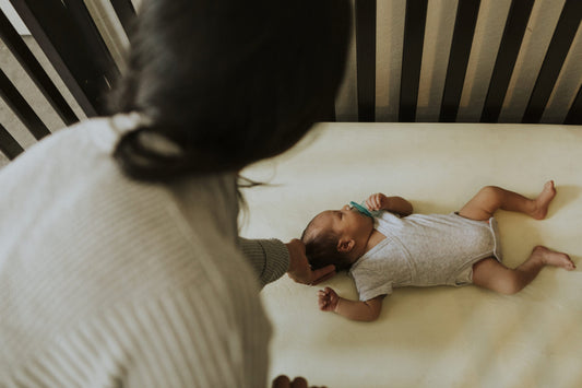 A mom is leaning into a crib and holding the back of her infant's head while the infact is laying down 