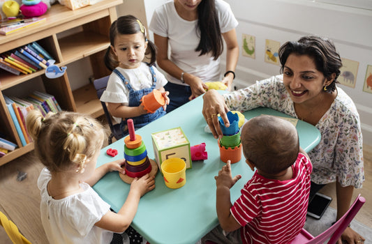 Classroom with two teachers and three little kids sitting around a small table with toys