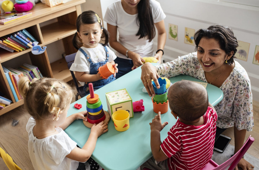 Classroom with two teachers and three little kids sitting around a small table with toys