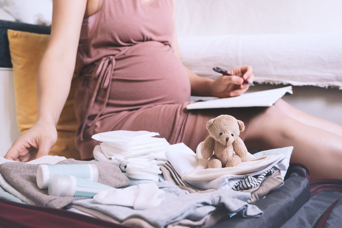 Image of a pregnant woman writing in a journal with various items next to her.