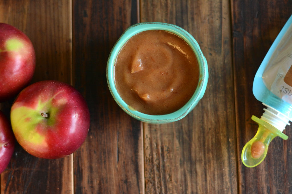 Apples to the left, a small bowl of homemade apple sauce in the center, and a Kiinde Storage Bag filled with apple sauce 
