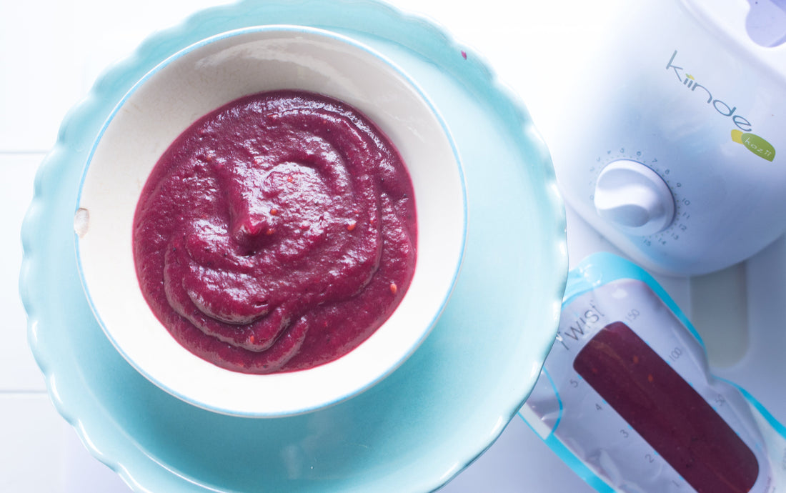 A bowl of blackberry apple puree next a Kiinde Kozii bottle warmer