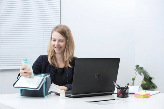 An image of a working mom pulling out Kiinde pouches from a cooler bag while sat at a desk with a laptop.