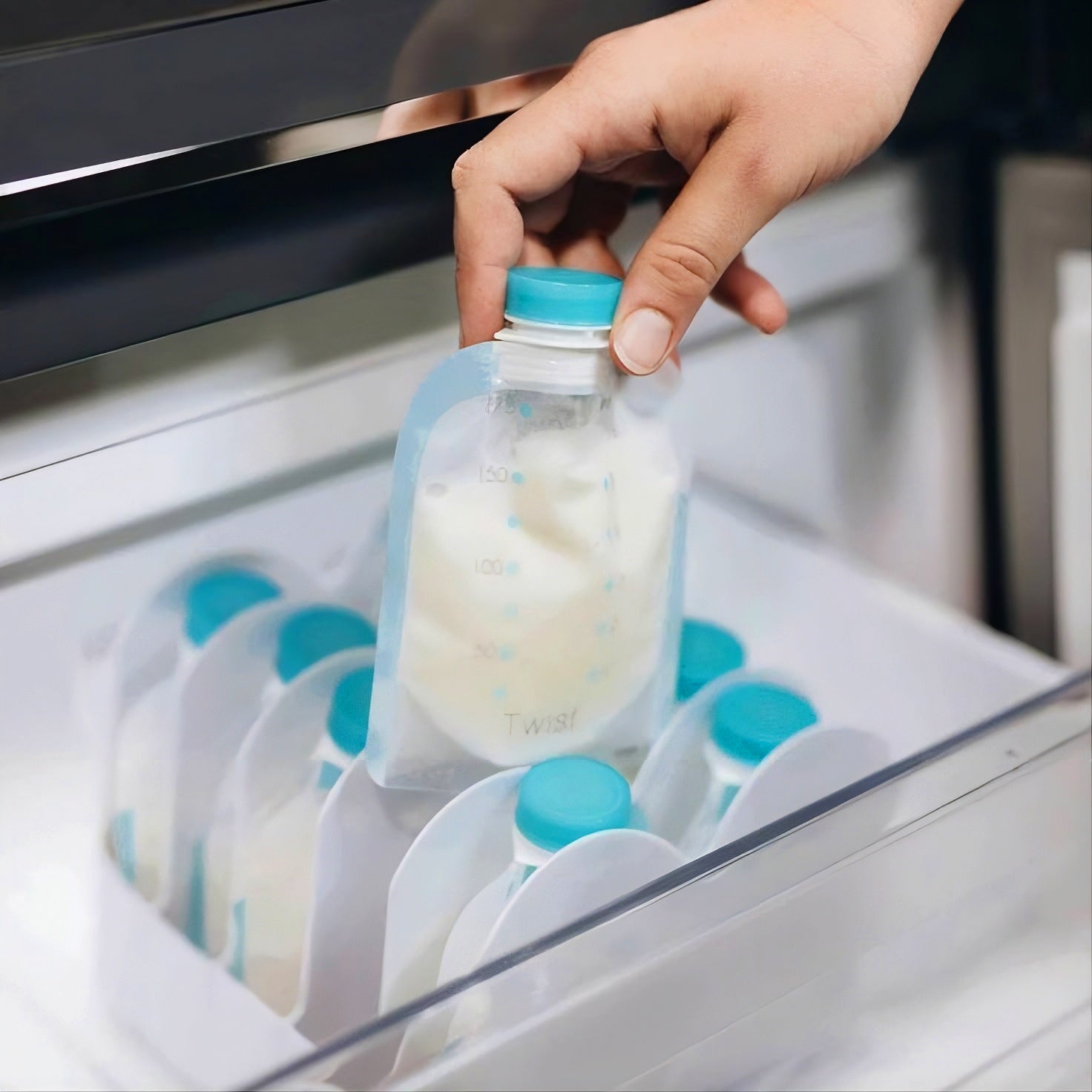 Kiinde Storage Bags in Kiinde Keeper organizer all inside a freezer. There is a hand pulling out one storage bag with milk inside.